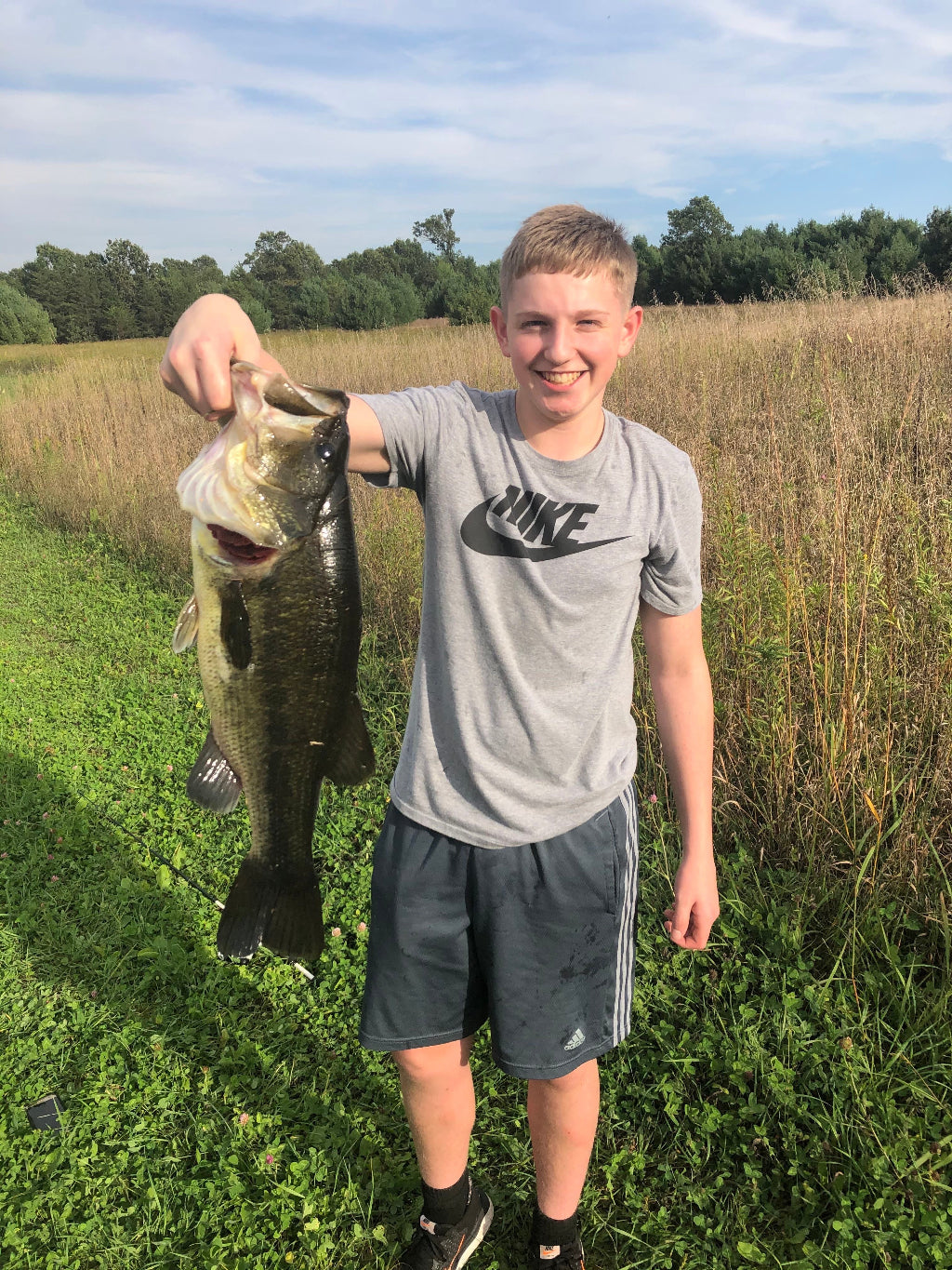 Person holding a large fish in a grassy field with trees in the background
