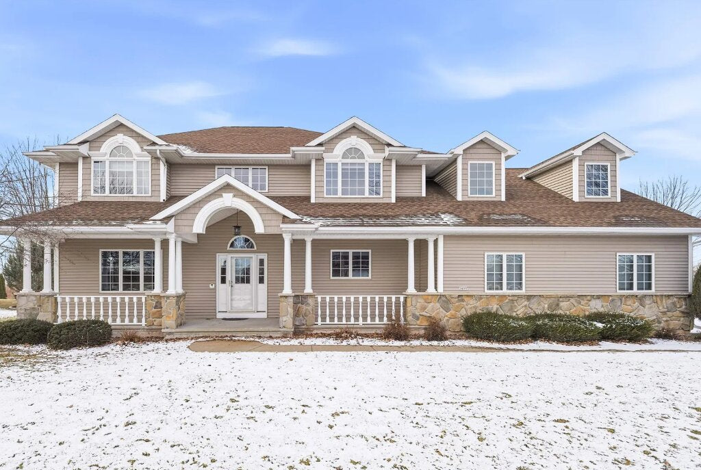 Spacious two-story home in Wisconsin with beige siding, covered front porch, stone foundation accents, and light snow covering the front yard.