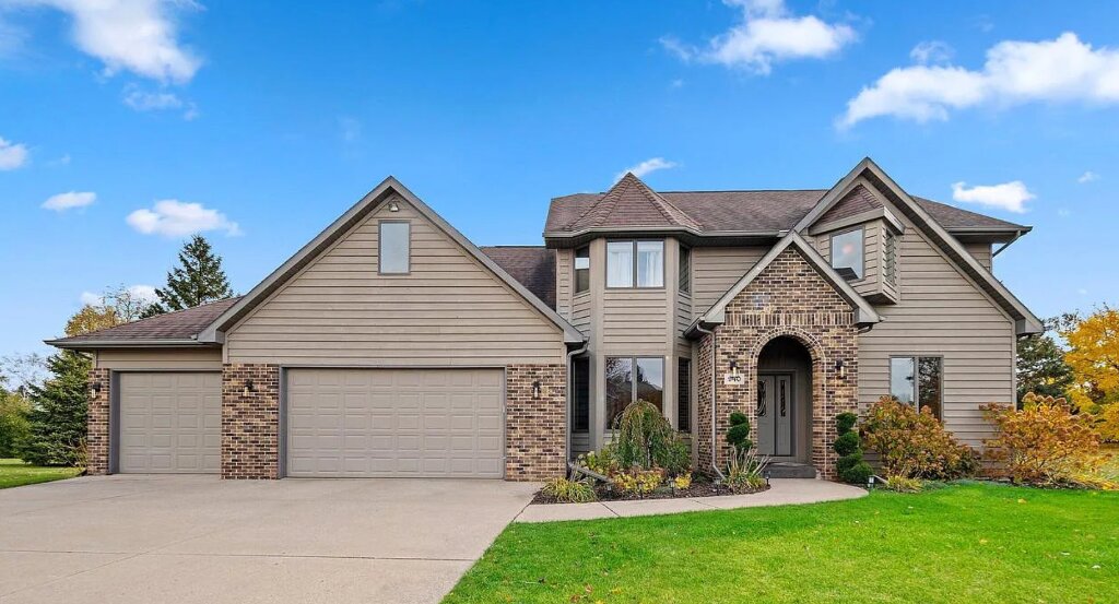 Beautiful suburban Wisconsin home with brick and siding exterior, arched front entry, landscaped yard, and three-car attached garage.